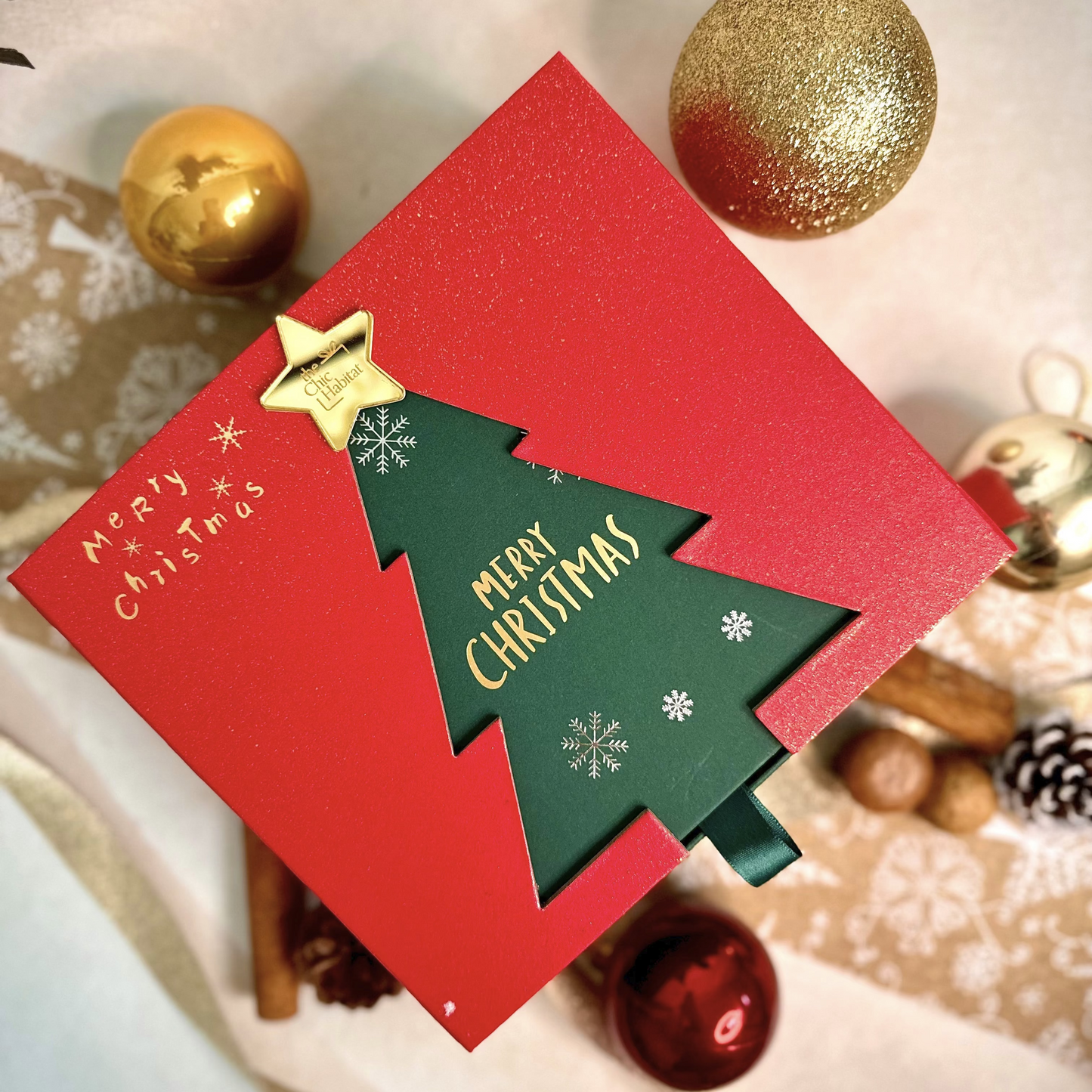 Red Christmas theme gift box with green Christmas tree design and 'Merry Christmas' text, surrounded by festive decorations.